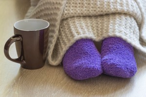Cold concept with teacup near the legs which are covered with fluffy warm blanket and wearing fluffy warm purple socks