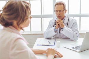 Handsome middle aged doctor is offering consultation to woman, at doctors office