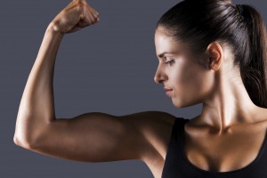 Perfect bicep. Beautiful young sporty woman examining her bicep while standing against grey background