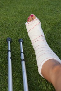 leg in plaster of a girl with polished fingernails and crutches on the grass